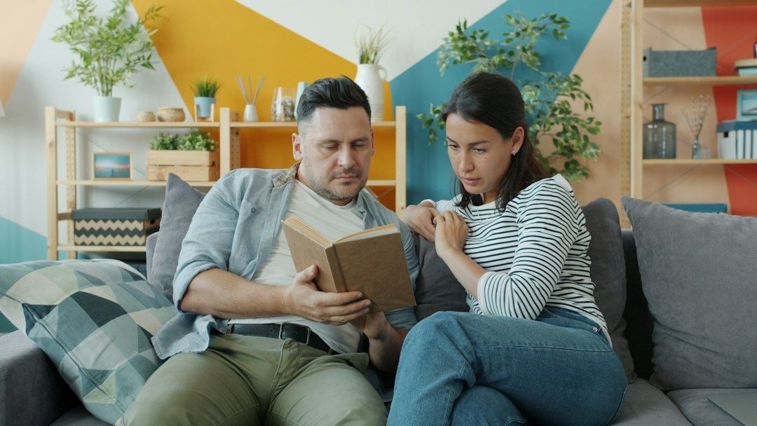 Twee volwassenen lezen samen een boek op de bank in een kleurrijke woonkamer