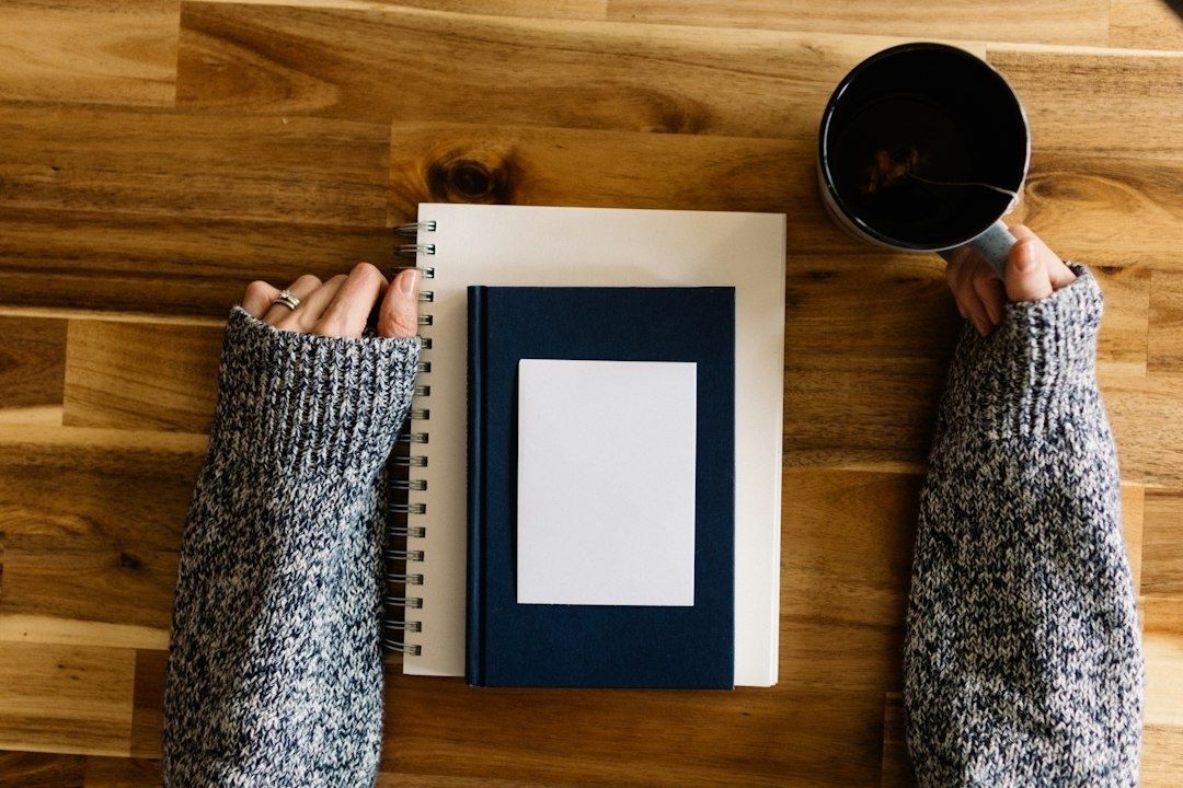 Handen bij een dicht boek, notitieboek en kop koffie op tafel